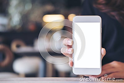 Mockup image of a woman holding and showing white mobile phone with blank screen on the table Stock Photo