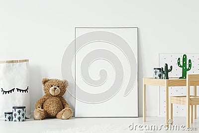 Mockup poster, teddy bear and material basket placed on the floor in white room interior with wooden table and small chair. Paste Stock Photo