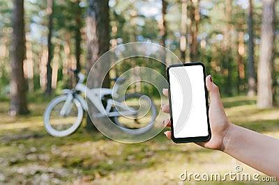 Mockup of a smartphone in a girl`s hand. Against the background of a bicycle in the forest Stock Photo