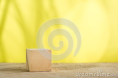 Mockup. Textured cube of beige surface on a yellow background with shadows from the leaves. Copy space Stock Photo