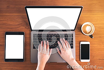 Mockup top view image of hands typing on laptop with blank white screen , mobile phone , tablet , coffee cup on vintage wood table Stock Photo