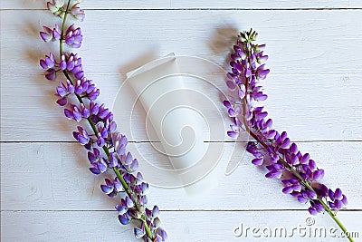 Mockup of unbranded white bottle tube for branding and purple flowers on white wooden table with horizontal boards. Top view Stock Photo