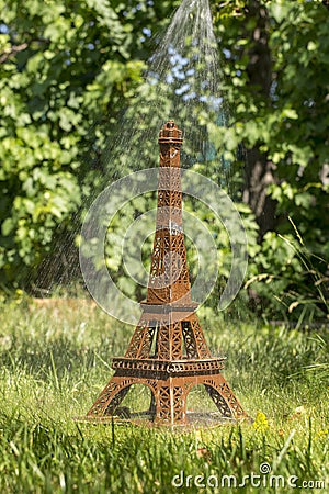 Model Eiffel Tower of cardboard on green grass under a stream of water Stock Photo