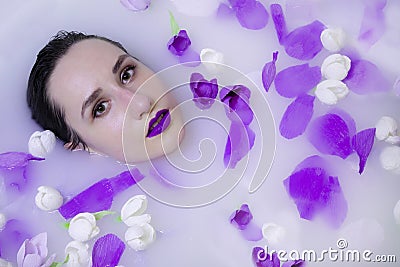 model girl with violet make-up in milk bath with violet flowers Stock Photo