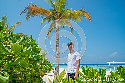 Model handsome young guy in white t-shirt standing on sandy beach at tropical island luxury resort Stock Photo