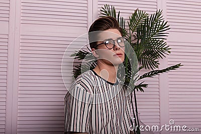 Model of a handsome young man in stylish wear in fashionable glasses with a amazing flower in a glass pot posing near a vintage Stock Photo