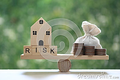 Model house with wording risk and money bag on wood scale seesaw on natural green background, Business investment and Risk Stock Photo