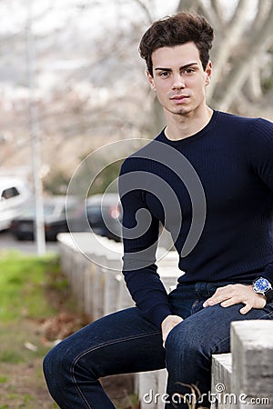 Model outdoor man, sitting on a low wall in the city. Stock Photo