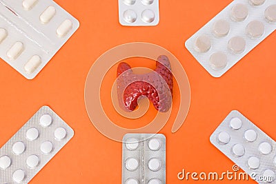 Model of thyroid gland surrounded by six blister packs with white pills inside in corners of image on orange background. Photo co Stock Photo