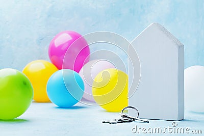 Model of a wooden house with bunch of keys and colorful air balloons on light background. Housewarming, moving, real estate. Stock Photo