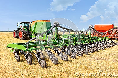 Agricultural seeders attached to tractors stand on yellow stubble in a wide field against a blue cloudy sky on a summer day Editorial Stock Photo