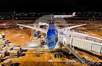 Modern airplane parked at the gate for boarding of passengers at an airport at night with motion of the ground vehicles. Vietnam Editorial Stock Photo