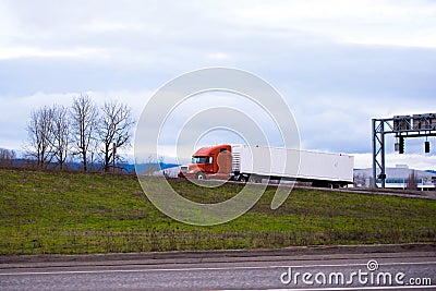 Modern big rig orange semi truck with long container trailer driving on the road Stock Photo