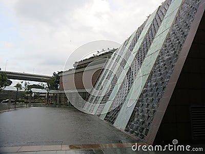 Modern Architects Singapore. Waterfall running down the wall of a building. Rain drops fall to the ground and form puddles. The co Stock Photo