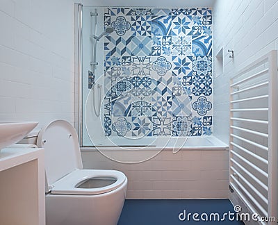 Modern bathroom with bath, toilet, niche in wall and basin unit, blue rubber floor and blue and white patchwork tiles Stock Photo