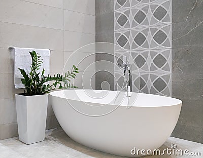 Modern bathroom interior design with white stone bathtub, grey tiles wall, ceramic flowerpot with green plant and hanger with Stock Photo