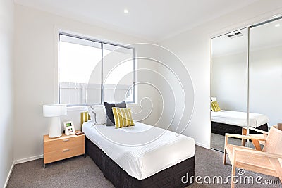 Modern bedroom with a single bed and white sheets near a mirror and to a chair Stock Photo