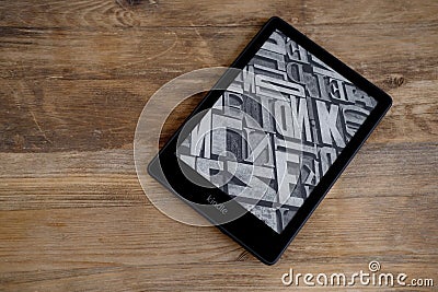 Modern black e-book reader, digital book Kindle, tablet computer device for displaying text electronically on old wooden table, Editorial Stock Photo