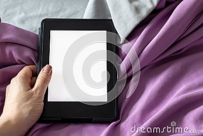 A modern black e-reader electronic book with a blank screen in female hand on a gray and purple bed. Mockup tablet on bedding Stock Photo