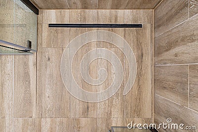 Modern black linear drain in a bathroom lined with ceramic tiles imitating wood, top view. Stock Photo