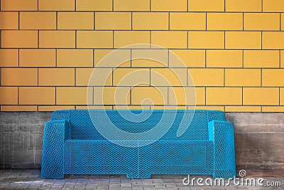 Modern blue metal sofa against yellow tile wall/ Urban furniture Stock Photo