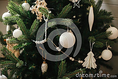 Modern boho christmas tree ornaments, white baubles, wooden garland, christmas lights close up. Atmospheric festive decorated Stock Photo