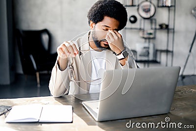 A modern businessman rubs his eyes in fatigue or exasperation while working on his laptop Stock Photo