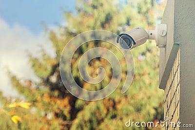 Modern CCTV camera on building wall, foliage background Stock Photo