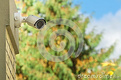 Modern CCTV security camera on building wall, foliage background Stock Photo