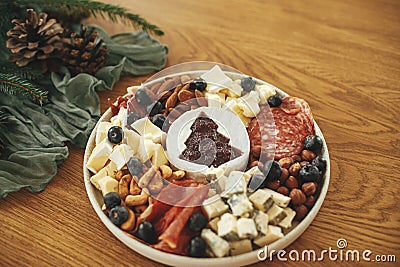 Modern cheese platter with different cheeses, salami and prosciutto, nuts and cranberry sauce as christmas tree on festive table. Stock Photo