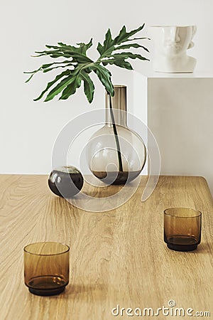 Modern composition of living room interior with wooden table, tropical leaf in vase, candelstick, decoration. Stock Photo