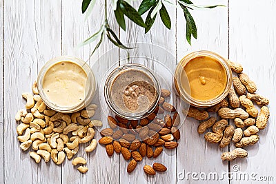 The modern concept of wellness and veganism. Jars of almond, cashew and peanut butter on a white wooden table with an olive branch Stock Photo