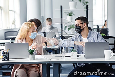 Modern high five at work after lockdown and new normal. Happy millennial man and woman in protective masks touch their Stock Photo