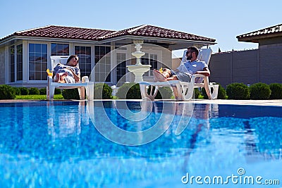 Modern couple getting tan under the sun near pool Stock Photo