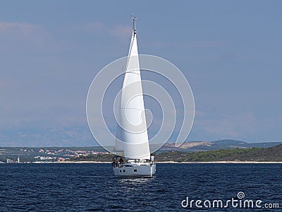 A modern cruise sailing yacht with a Bermuda sloop-type rig goes past the green coast of the Croatian Riviera on a sunny summer da Editorial Stock Photo