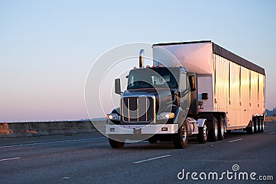 Dark big rig semi truck with bulk trailer running on highway in Stock Photo