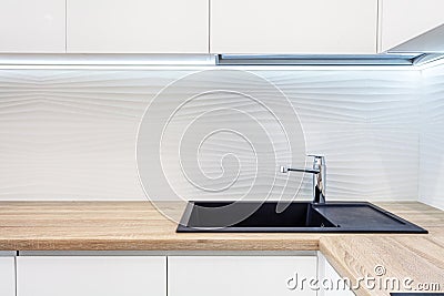 Modern designer chrome water tap over black new kitchen sink. The working area of the kitchen surface is made of wood. Table top m Stock Photo