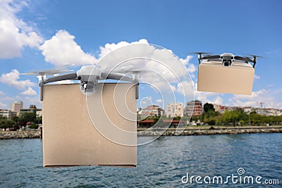 Modern drones with carton boxes flying above sea on sunny day. Delivery service Stock Photo