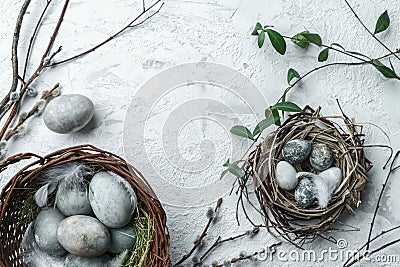 Modern Easter eggs in wicker basket on white textured background with nest, feathers and spring flowers. Happy Easter holiday, top Stock Photo