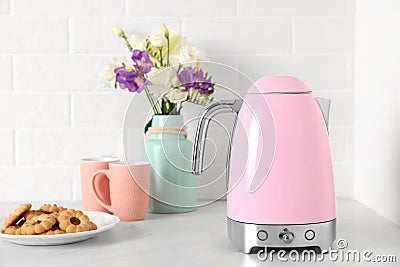 Modern electric kettle, bouquet, cookies and cups on counter in kitchen Stock Photo