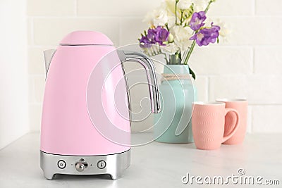 Electric kettle, bouquet and cups on counter in kitchen Stock Photo