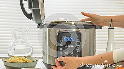 Modern electric multi cooker close up on kitchen table. Woman pushing button Stock Photo