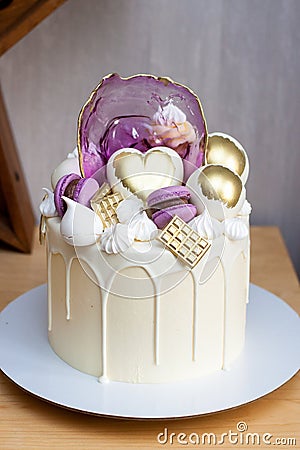 Modern elegant cake with melted white chocolate, golden heart and chocolate balls, macaroons, meringue and caramel. Stock Photo