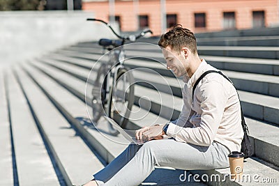 Modern employee sitting on stairs and networking outdoors with takeaway coffee and bike Stock Photo