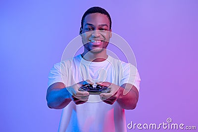 Modern Entertainment. Smiling Black Guy In Neon Light With Joystick In Hands Stock Photo