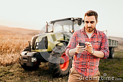 Modern farmer working and harvesting using smartphone in modern agriculture with tractor background Stock Photo