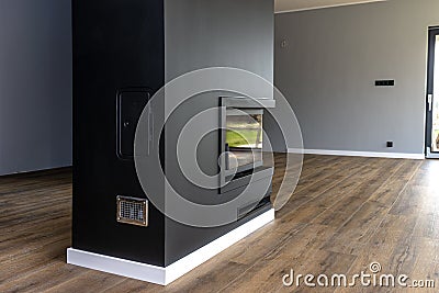 A modern fireplace with a closed combustion chamber standing in the living room, painted black, with a corner pane covered with so Stock Photo