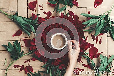 modern floral instagram blogging image. hand holding stylish coffee and beautiful red peonies on rustic wooden background flat la Stock Photo