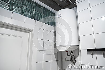 Modern gas tanked boiler in bathroom. Household budget water heater hanging on the wall in boiler room. Common electric storage Stock Photo