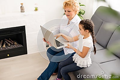 modern grandmother teaching grandchild how to use laptop computer at home Editorial Stock Photo